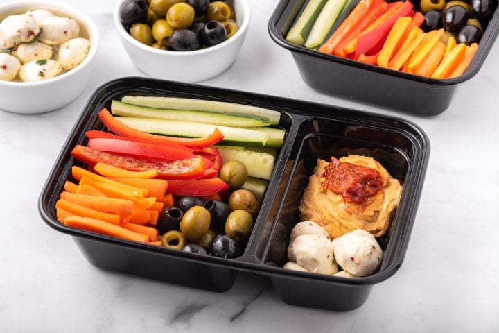 Mediterranean snack box with olives, carrots, hummus, cucumbers, tomatoes, and mozzarella cheese balls.