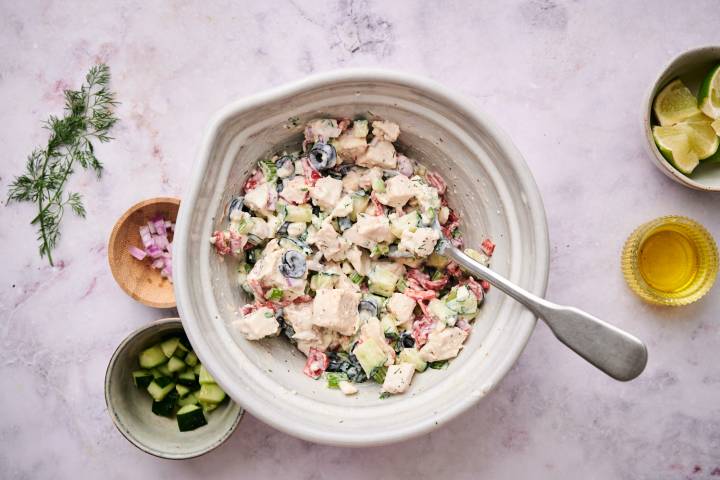 Mediterranean chicken salad with cucumbers, roasted red peppers, dill, parsley, and red onion in a bowl with lettuce on the side.