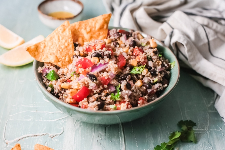 Mexican quinoa with black beans, corn, tomatoes, onion, taco seasoning, and cilantro served in a bowl with chips.
