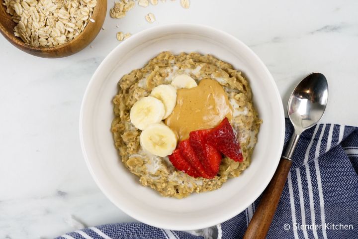 Banana Peanut Butter Microwave Oatmeal in a bowl with rolled oats, bananas, peanut butter, and strawberries.
