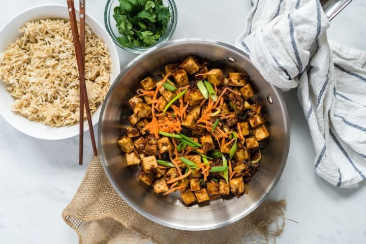 Mongolian tofu in a skillet with carrots, green onions, crispy tofu, and a sweet and spicy sauce.