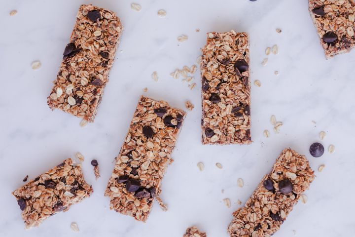 No bake granola bars with rolled oats, almond butter, chocolate chips, chia seeds, and flax seeds on a marble board.