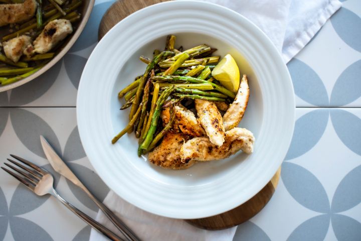 One pan lemon garlic chicken and asparagus served with fresh lemons in a bowl and in a skillet.
