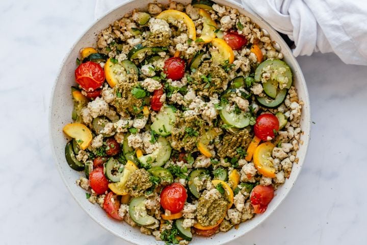 Ground turkey, zucchini, yellow squash, and cherry tomatoes in a skillet and topped with pesto.