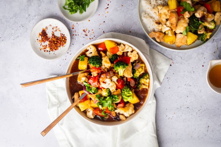 Pineapple chicken stir fry with chicken breast, fresh pineapple, broccoli, cauliflower, and red bell peppers in a bowl with rice.