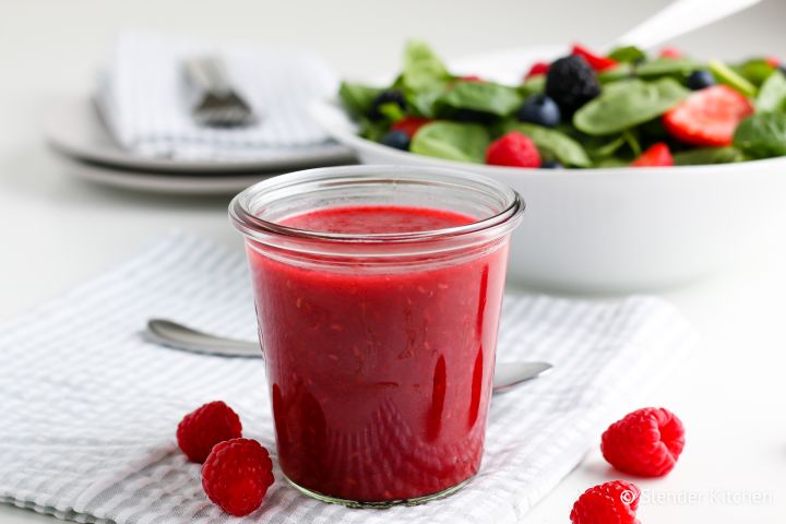 Raspberry vinaigrette dressing in a glass jar with raspberries and a green salad.