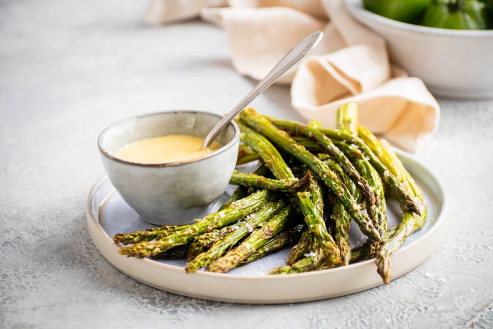 Roasted asparagus with olive oil, salt, and pepper served on a plate with hollandaise sauce.
