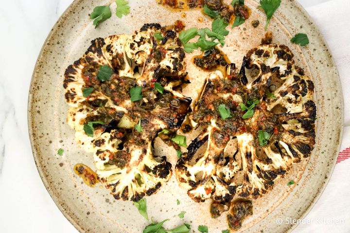Roasted cauliflower steaks with chimichurri sauce drizzled on top.