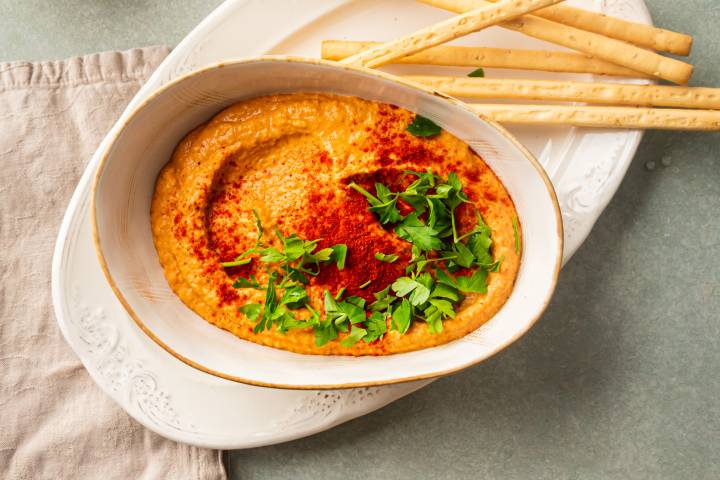 Roasted red pepper hummus made with chickpeas, tahini, garlic, lemon, and olive oil in a bowl with cilantro and paprika.