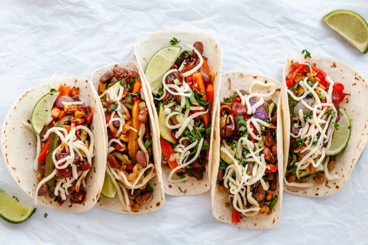 Roasted vegetable fajitas with bell peppers, onions, corn, carrots, zucchini, and pinto beans in tortillas with cheese and limes.