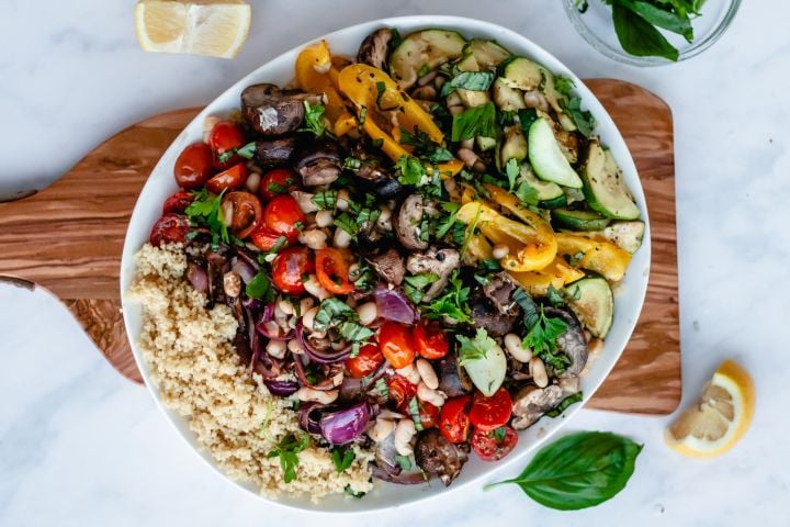 Roasted vegetables with couscous, fresh parsley, and fresh basil served with lemon and balsamic vinegar on a white plate.