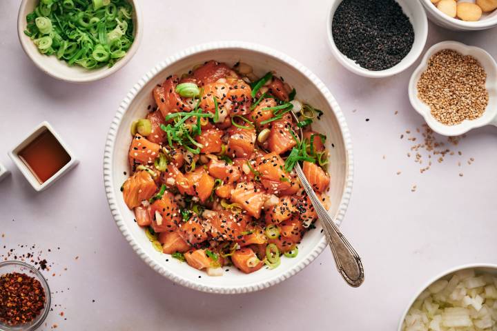Salmon poke in a bowl with soy sauce, sesame oil, green onions, white onions, and sesame seeds.