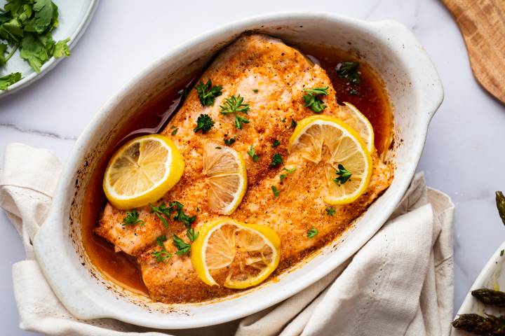 Salmon recipe for lemon pepper salmon served in a white baking dish with sliced lemons and parsley.