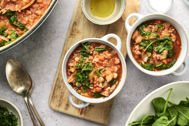 Sausage, white bean, and spinach soup with fresh parsley served in a blue ceramic bowl.