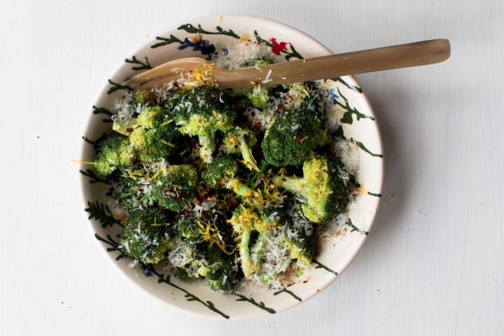 Sauteed broccoli with Parmesan cheese, lemon zest, red pepper flakes, and olive oil in a ceramic bowl with a wooden spoon.