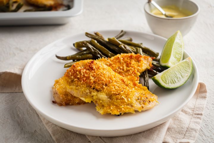Sheet pan lemon pepper chicken coated with breadcrumbs and Parmesan cheese on a plate with roasted green beans,