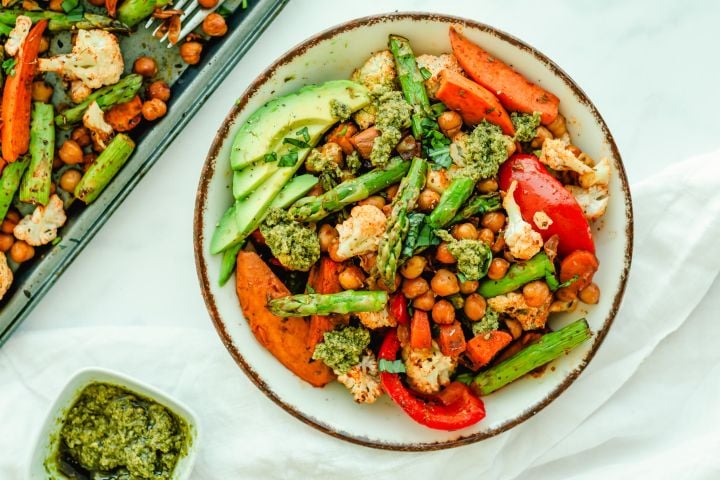 Sheet pan pesto chickpeas and vegetables on a plate with asparagus, sweet potatoes, chickpeas, carrots, cauliflower, and peppers.