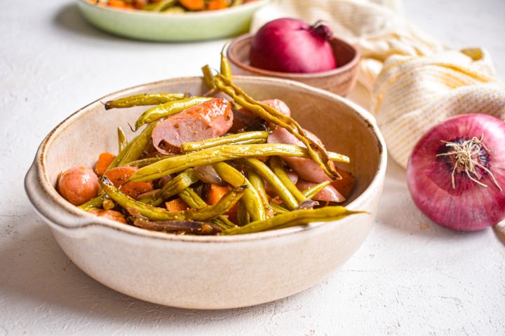 Sheet pan sausages, sweet potatoes, green beans, and red onions in a bowl with spices.