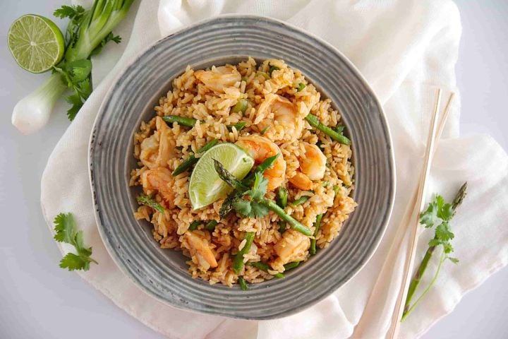 Shrimp fried rice with asparagus, cilantro, and a lime wedge in a bowl.