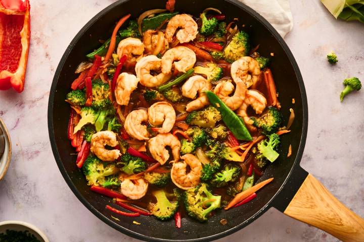 Shrimp stir fry with broccoli, snap peas, peppers, onions, and carrots in a skillet with stir fry sauce.