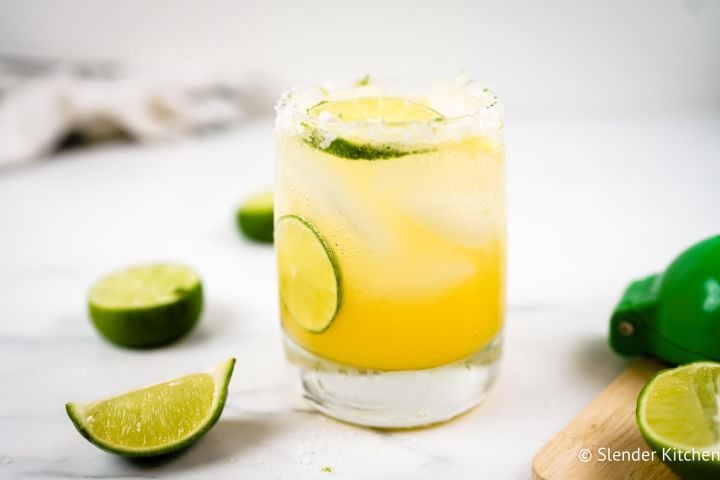 Skinny margaritas in a glass with a salted rim, fresh limes, and orange juice.