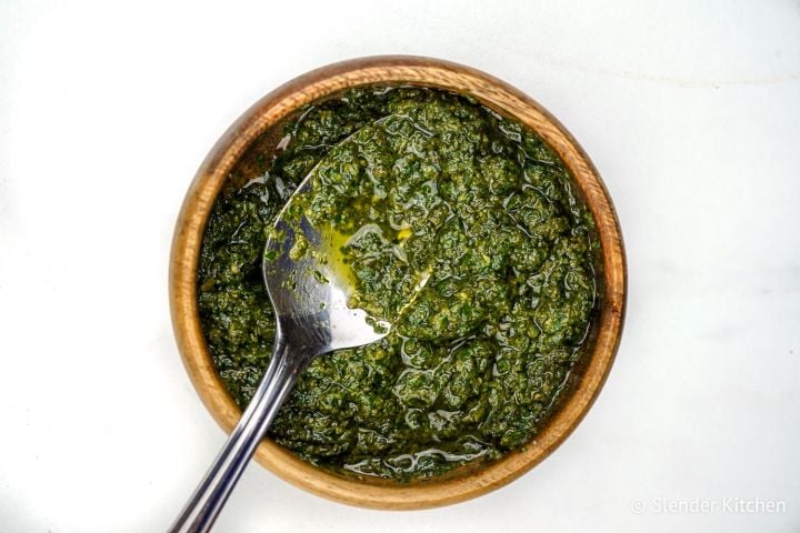 Skinny pesto in a wooden bowl with olive oil and a spoon.