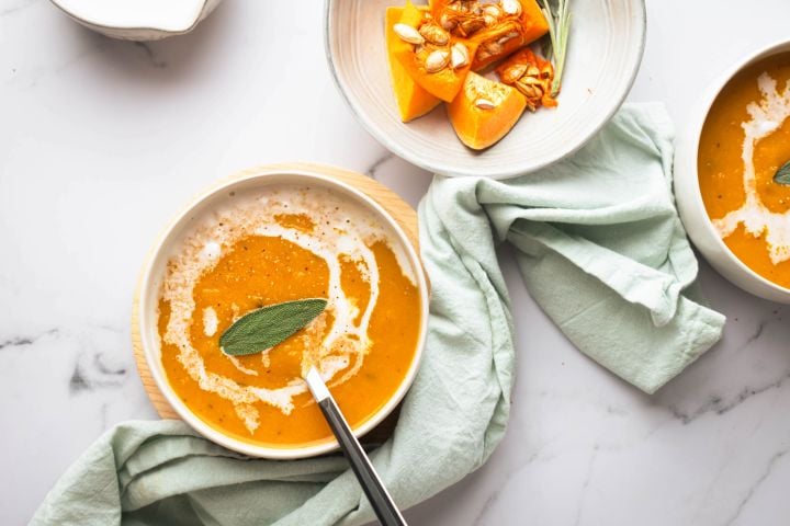 Slow cooker butternut squash soup in two bowls with a sage leaf on top.