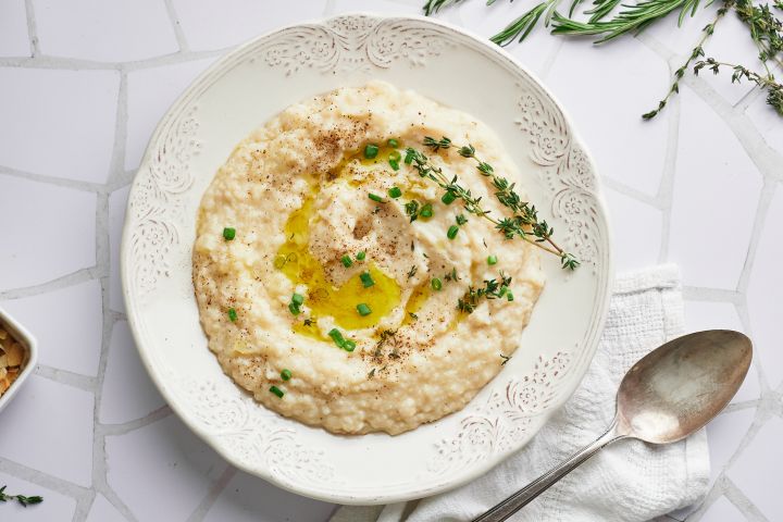 Slow cooker cauliflower mashed potatoes made with potatoes and cauliflower florets served in a bowl with fresh herbs and olive oil.