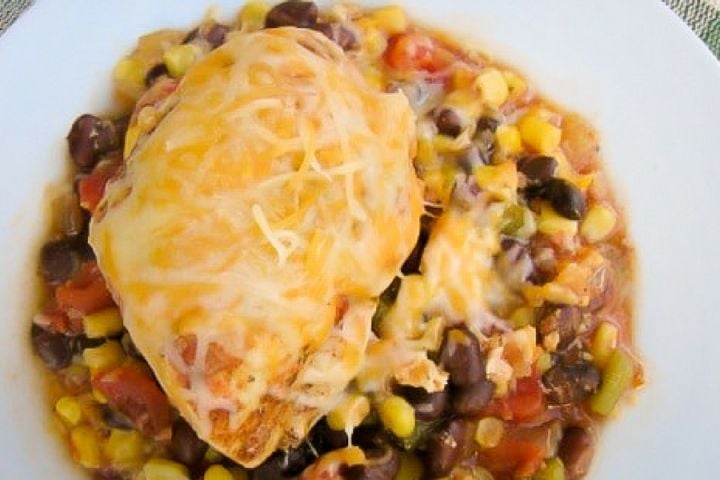Slow Cooker Southwestern Chicken on a bed of black beans and corn with cheese melted on top.