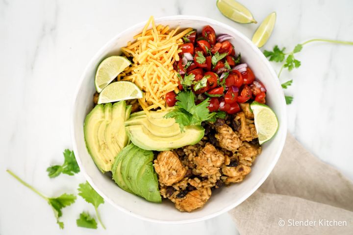 Slow cooker chicken burrito bowls with chicken breast, rice, black beans, avocado, and cheese in a bowl.