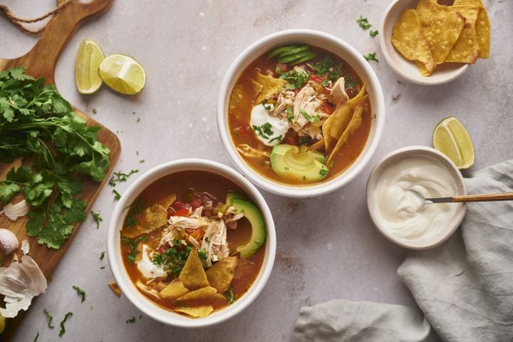 Slow Cooker Chicken Fajita Soup in tow bowls with shredded chicken, bell peppers, onions tortilla chips, and avocado.