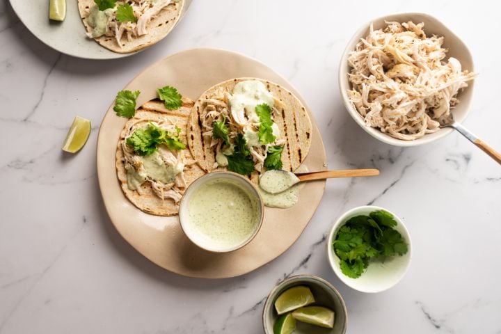 Slow cooker jalapeno chicken tacos with cilantro and Greek yogurt sauce served on corn tortillas.
