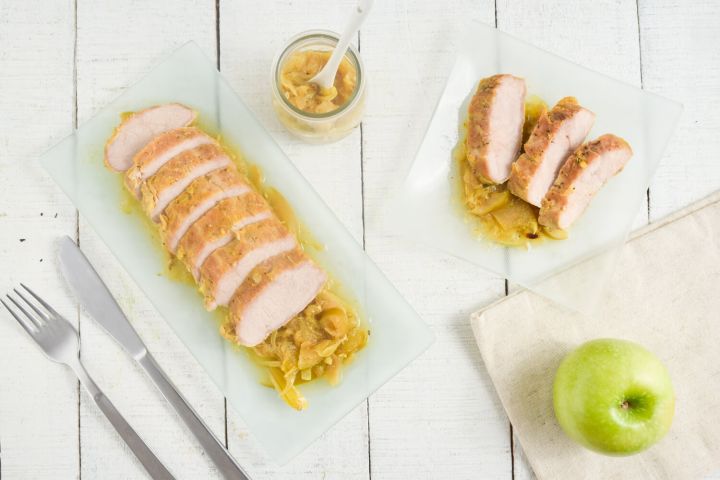 Slow Cooker Pork Tenderloin on a bed of apples and onions with a green apple on the side.