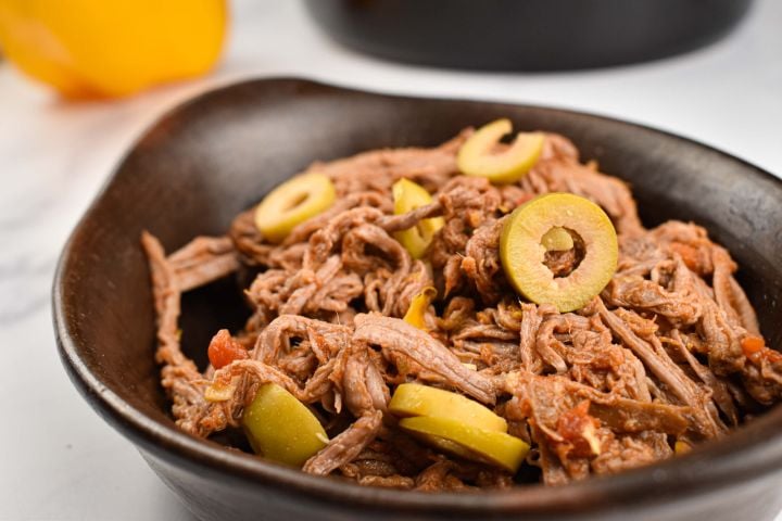 Slow cooker ropa vieja with peppers, onions, tomatoes, and olives in a black dish.