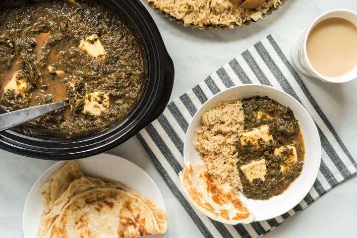 Slow cooker saag paneer on a plate with brown rice and Naan bread with the slow cooker on the side.