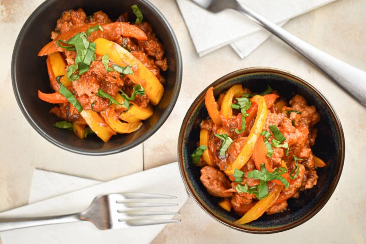 Slow cooker sausage and peppers in a homemade tomato sauce in two bowls with forks.