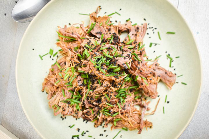 Slow Cooker Sesame Beef in a bowl with sliced green onions and sesame seeds.