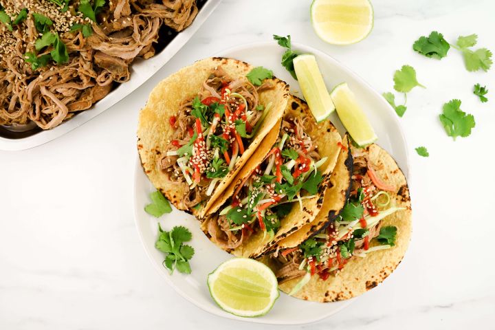 Slow Cooker Korean Pork served in corn tortillas with slaw and hot sauce.
