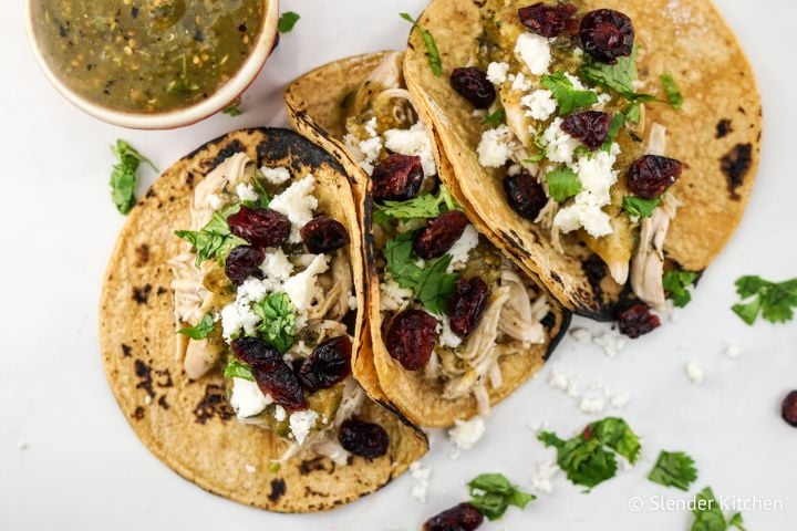 Slow cooker turkey tacos served in corn tortillas with shredded turkey, green salsa, cotija cheese, and dried cranberries.