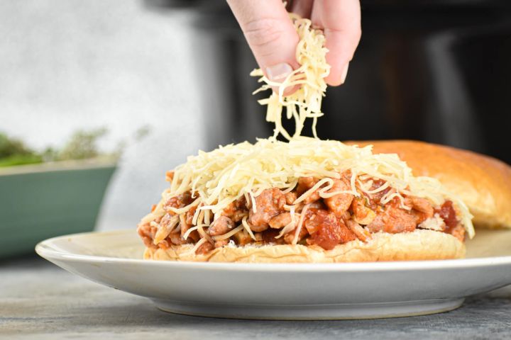 Slow cooker Tuscan turkey sloppy joes on a roll with shredded cheese.