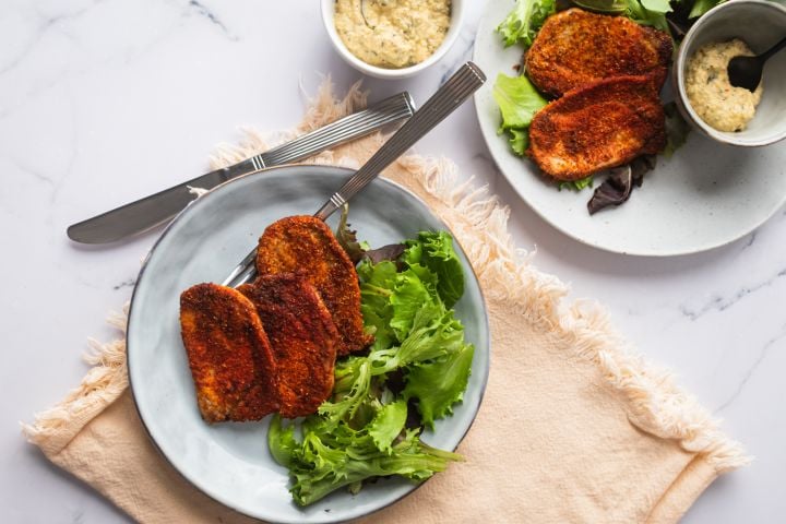 Spice crusted pork chops on a plate with mustard sauce and salad greens.