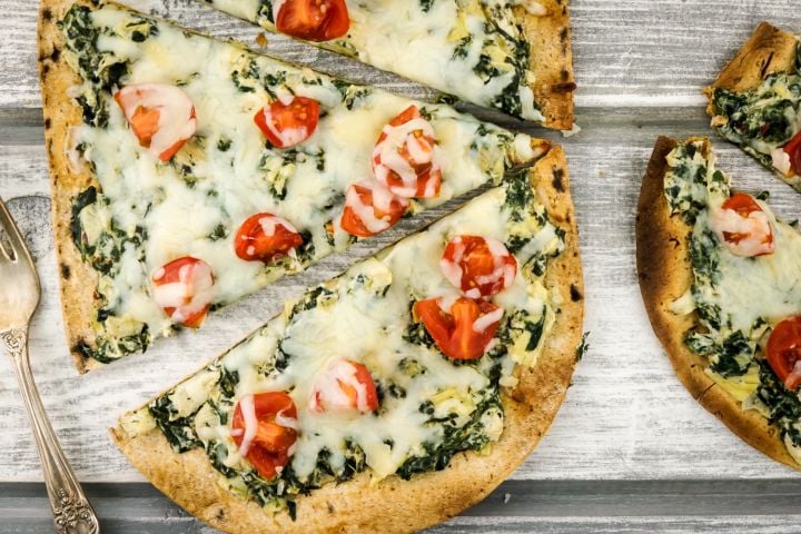 Spinach artichoke pizza with cherry tomatoes and melted cheese.