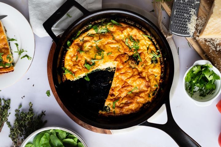 Spinach frittata with cheddar and Parmesan cheese in a cast iron skillet.