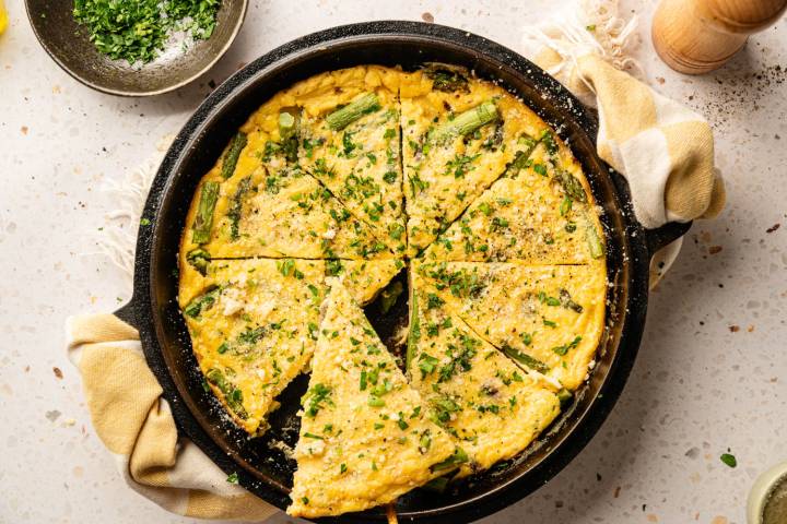 A freshly baked frittata with asparagus and herbs, sliced into wedges in a cast iron skillet.
