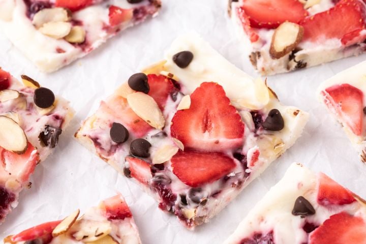 Strawberry frozen yogurt bark with chocolate chips, sliced almonds, and raspberry jelly broken into squares.