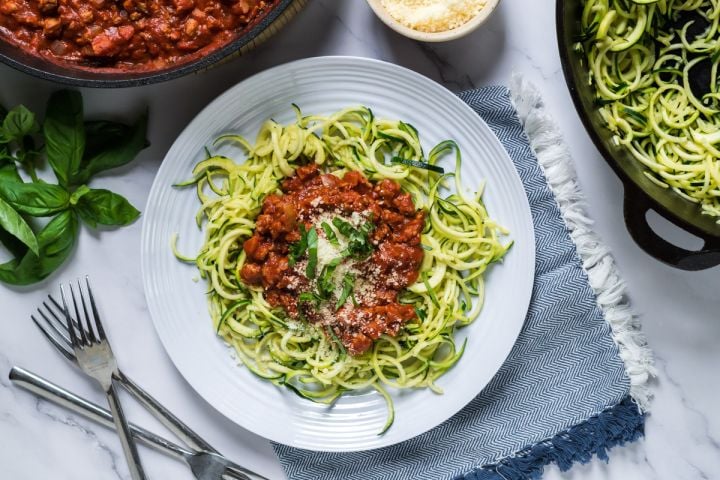 Tomato basil zucchini noodles with ground turkey served on a plate with basil and Parmesan cheese.