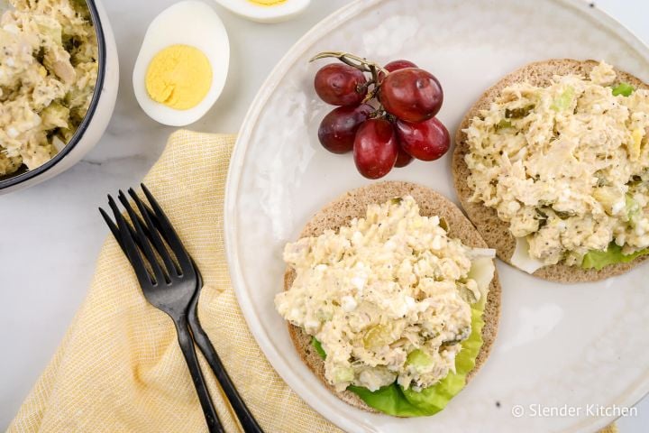 Tuna egg salad on a sandwich thin with red grapes and lettuce.