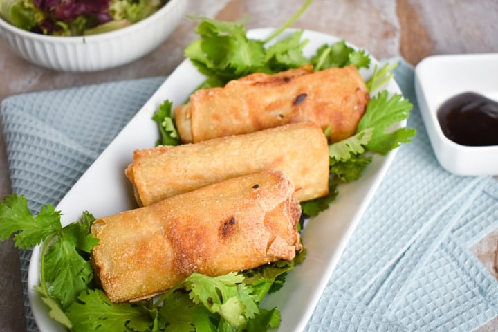 Vegetable egg rolls with crispy edges filled with cabbage, carrots, and mushrooms on a plate with herbs.