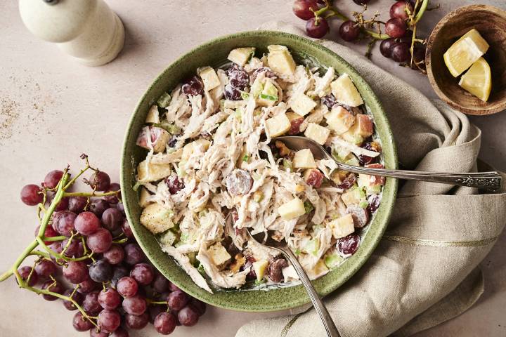 Overhead view of Waldorf chicken salad in a green bowl, made with shredded chicken, red grapes, celery, apples, and walnuts, served with two spoons.