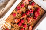 Baked rolled oats with bananas, old fashioned oats, and almond milk in a baking dish with berries and chocolate chips.